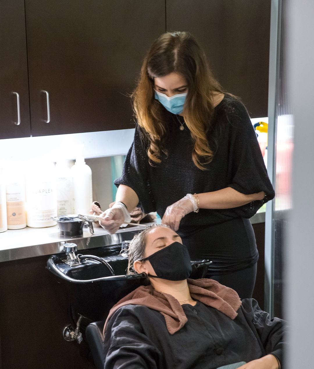 A stylist in a salon working colour into a client's hair at a black shampoo basin