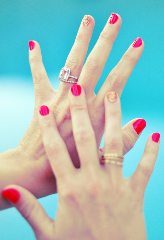 Two hands with bright pink and glitter nail polish held against a turquoise background