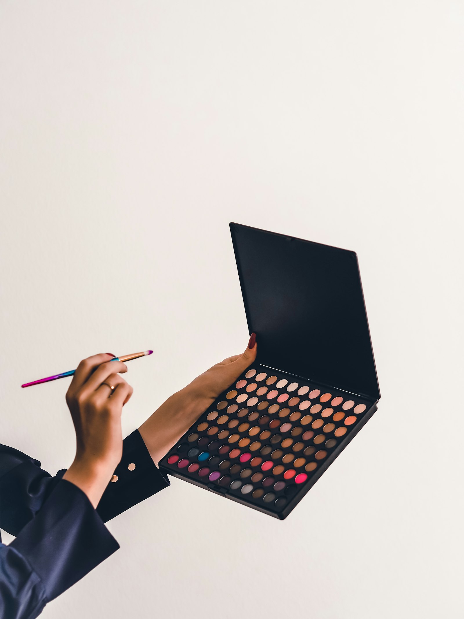 A person holding an open 35-pan eyeshadow palette and a brush against a pale background
