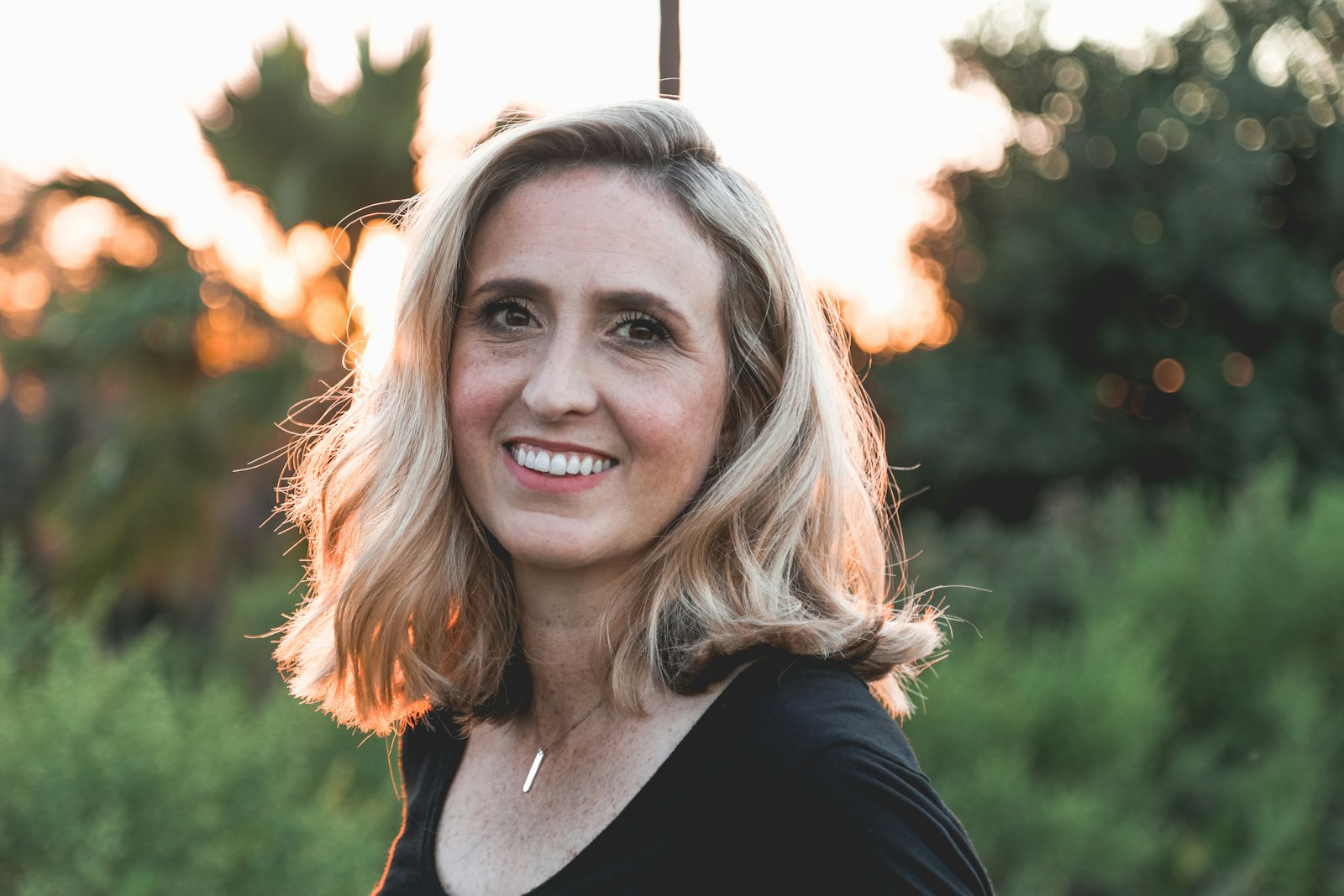 A woman with shoulder-length blonde hair outdoors in warm evening light