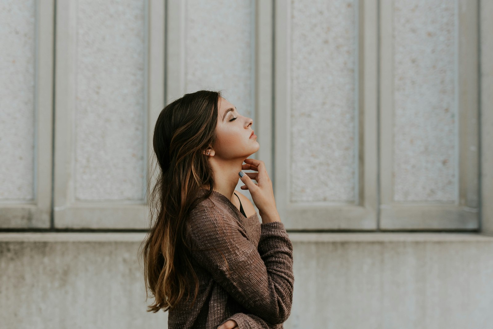 A profile portrait of a woman with long wavy hair in a brown knit top, eyes closed