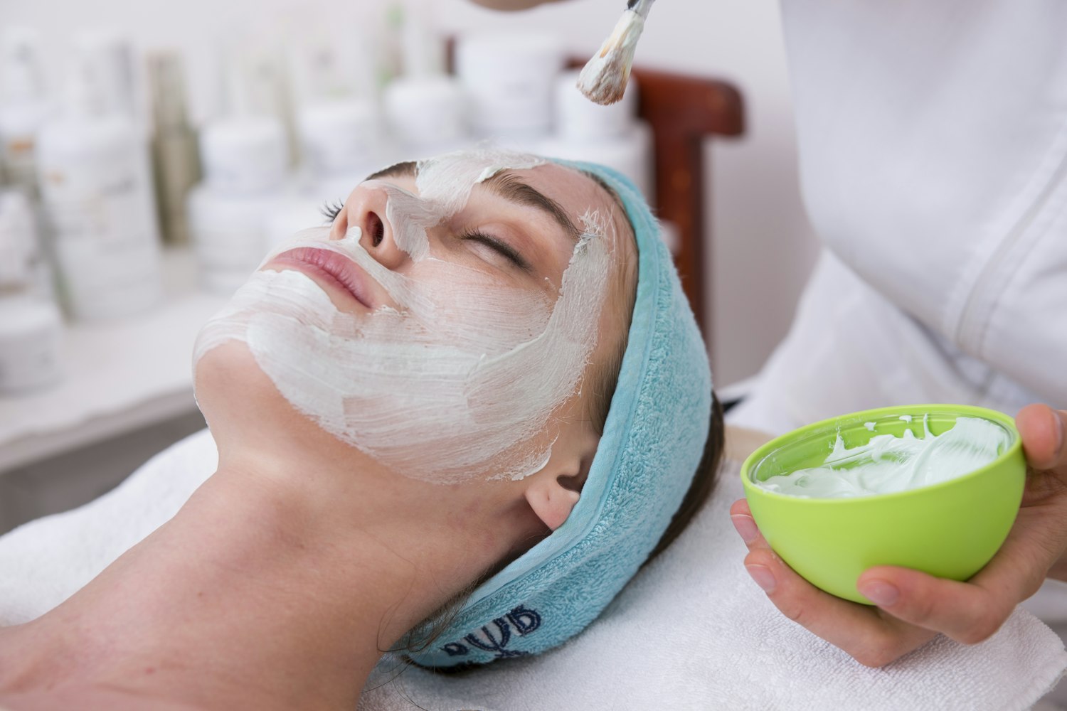 A woman wearing a white sheet mask holding half an avocado against a warm brown background