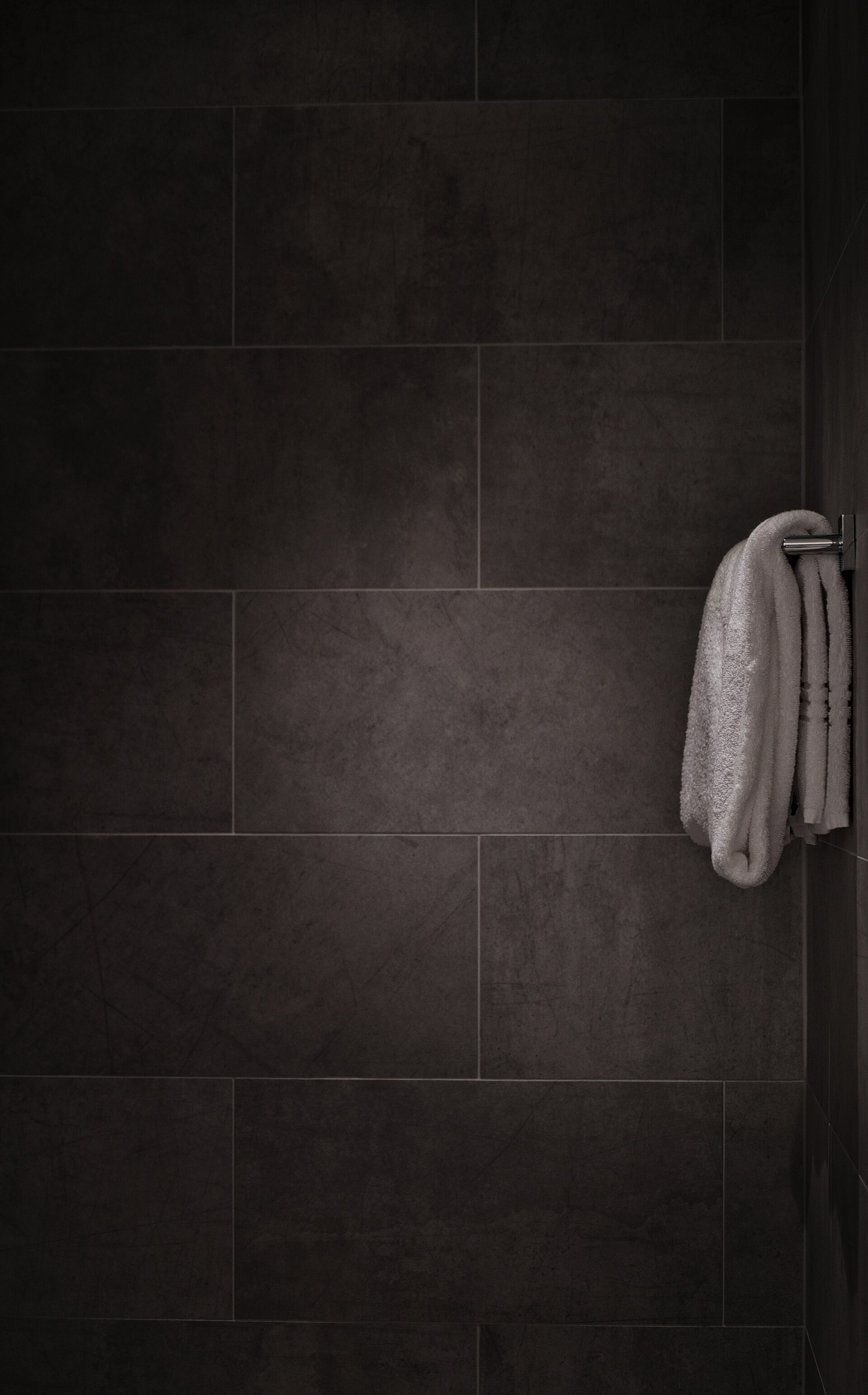 A white towel hanging on a rail against dark grey tiled bathroom walls