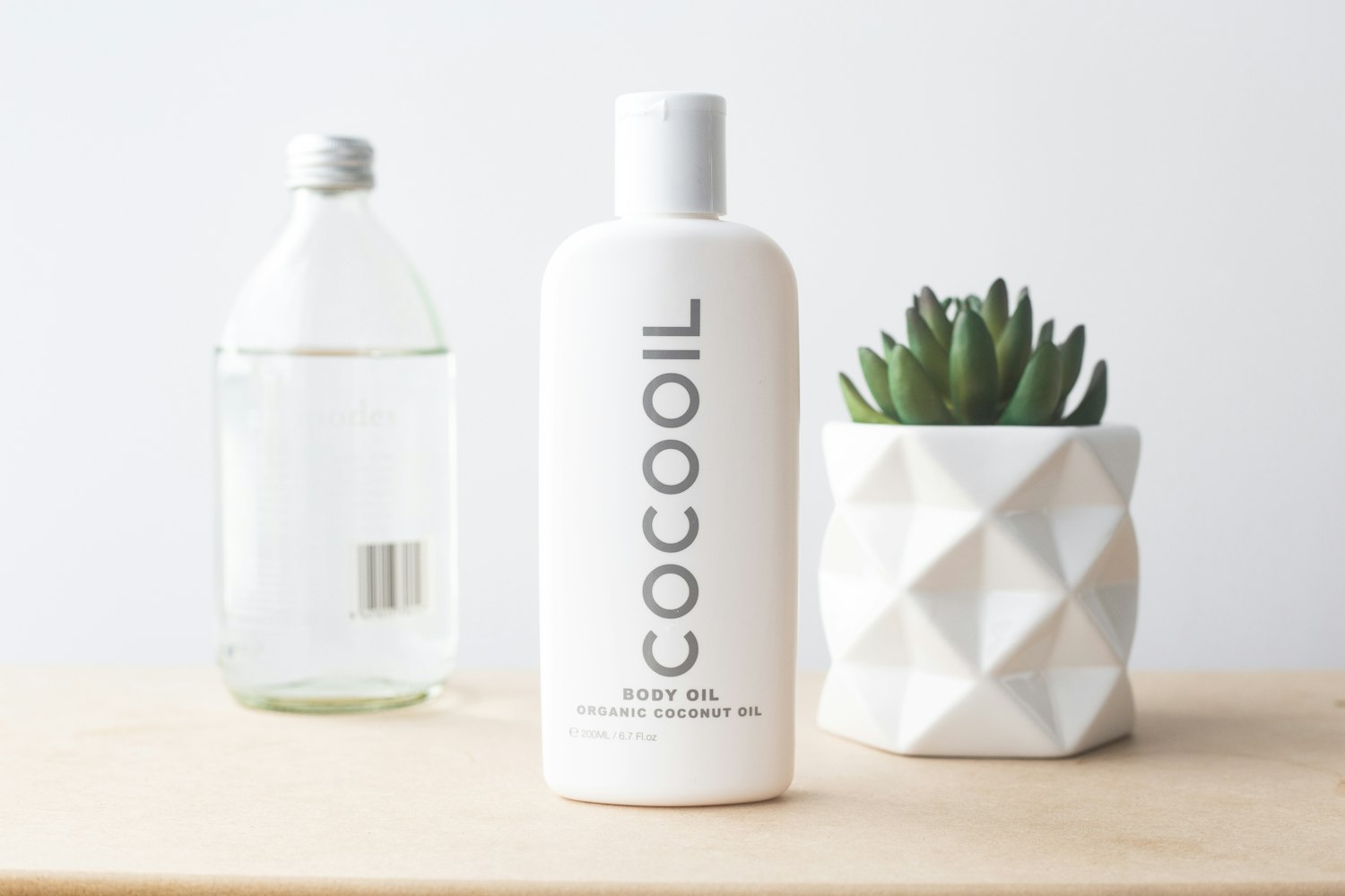 A bottle of organic coconut body oil beside a small succulent in a geometric white planter